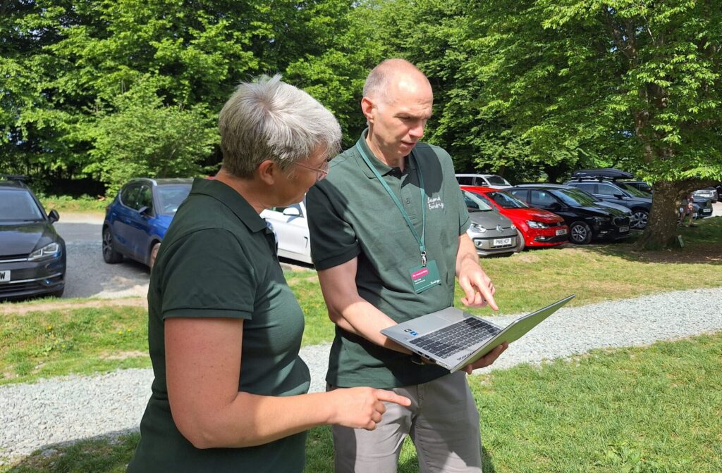Two people stood outside in the sunshine, looking at a laptop