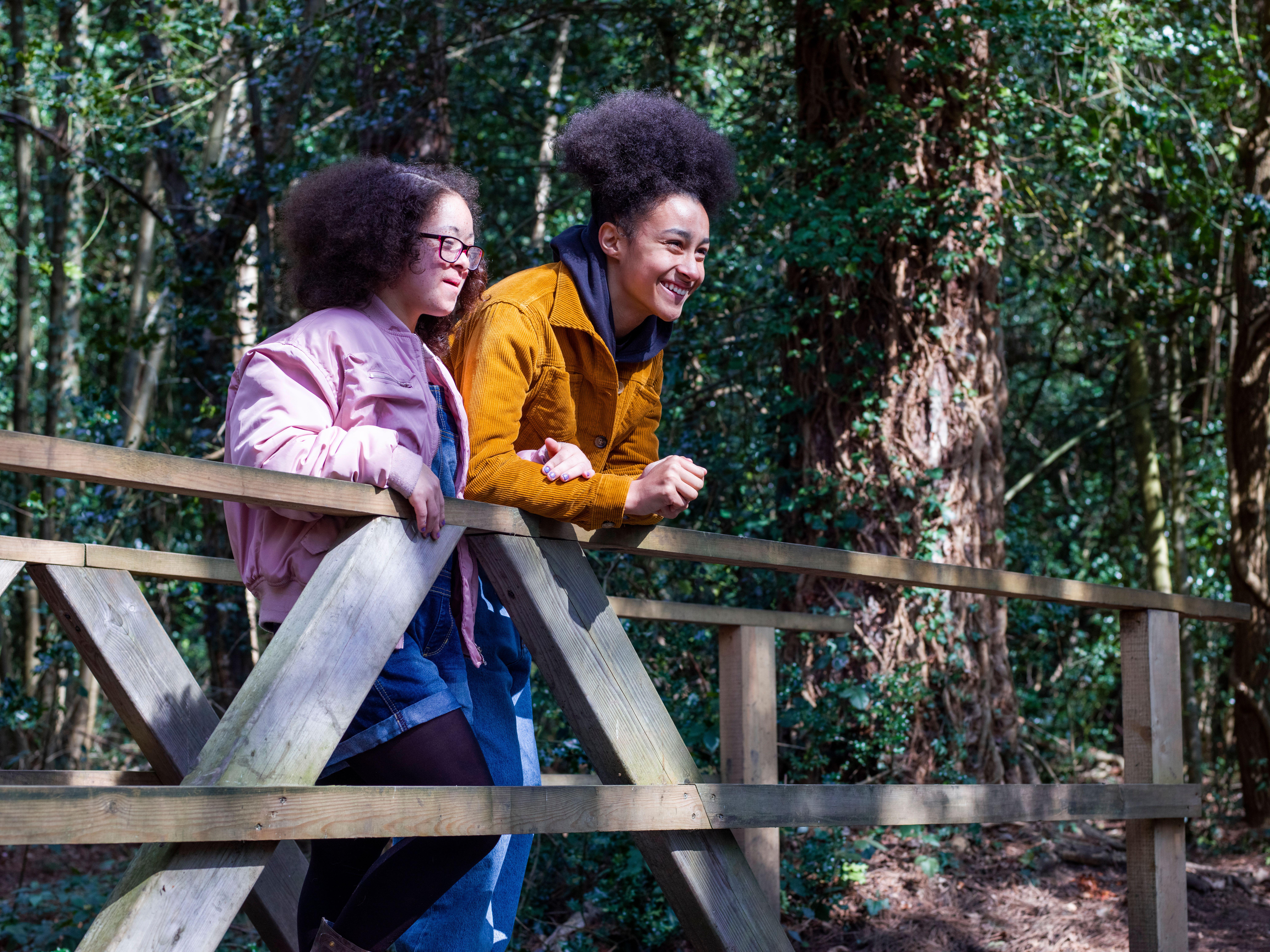 Two people stood on a bridge in woodland, smiling