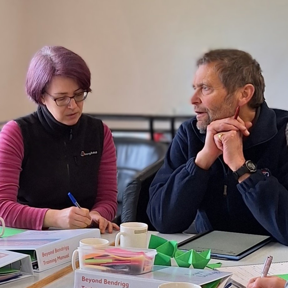 Two people sitting at a desk which is covered in training materials