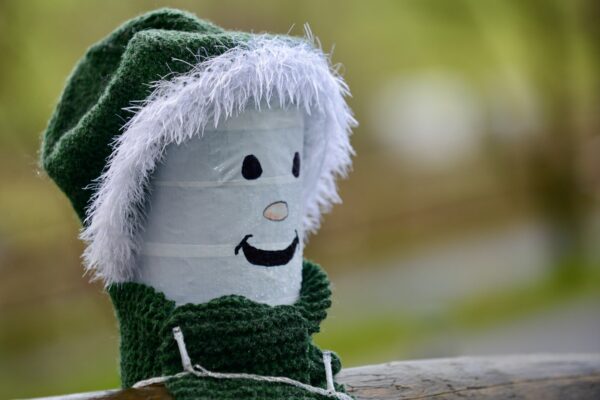Fence post decorated as a snowman wearing a green santa hat and a smiley face