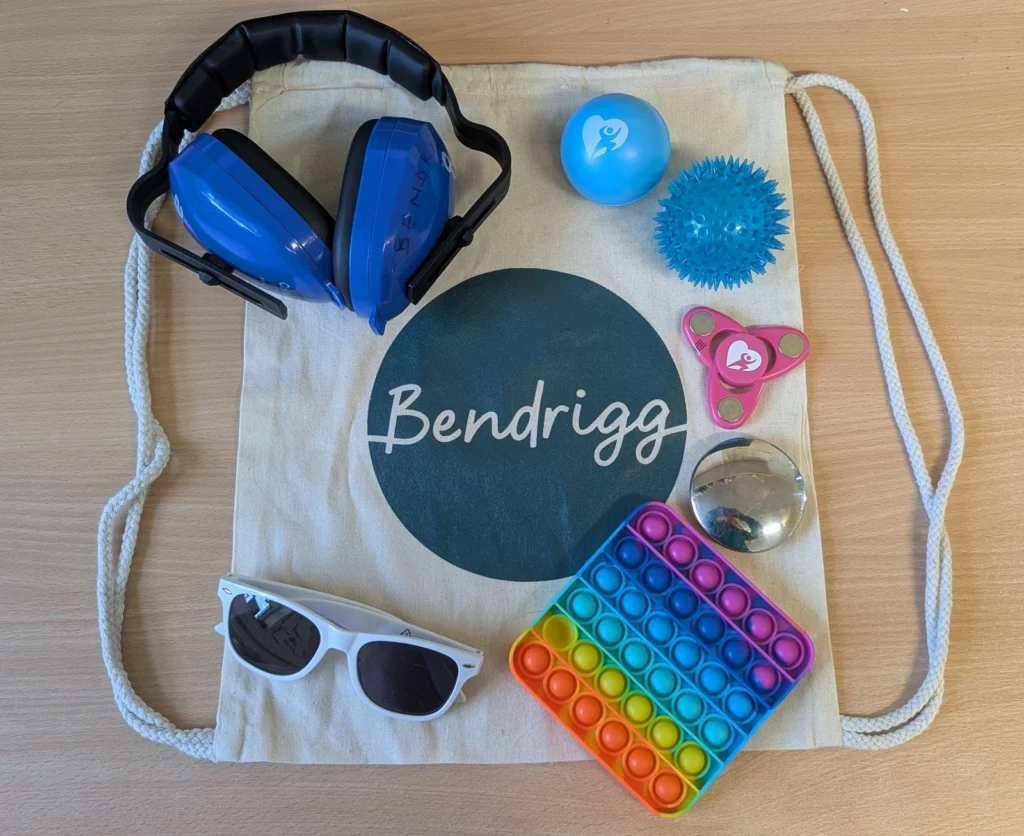 Sensory tools arranged on a Bendrigg draw sting back, Ear defenders, stress balls, fidget spinner and sunglasses